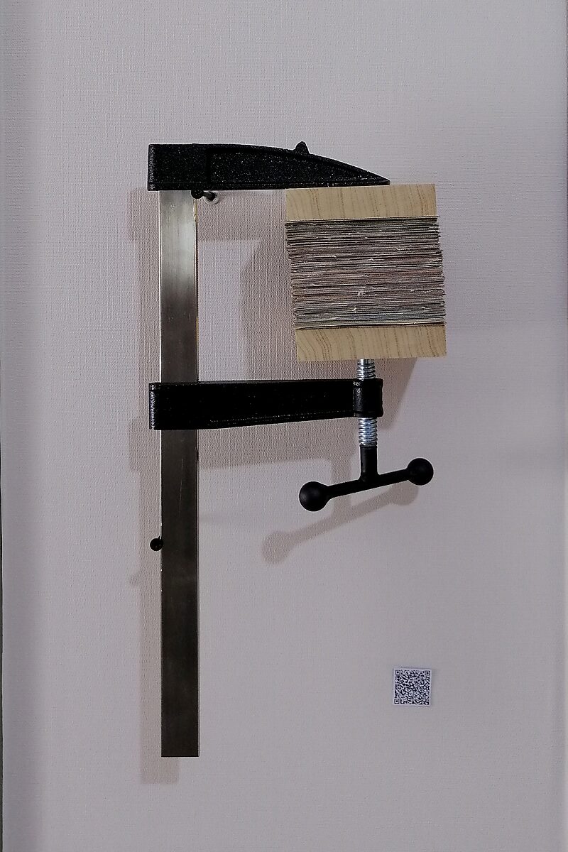 Schilderijen.zip — een ander exemplaar van het samengeperste schilderijblok in een lijmklem; de gelaagde randen van het doek zijn zichtbaar als een compacte stapel verf- en canvaslagen.