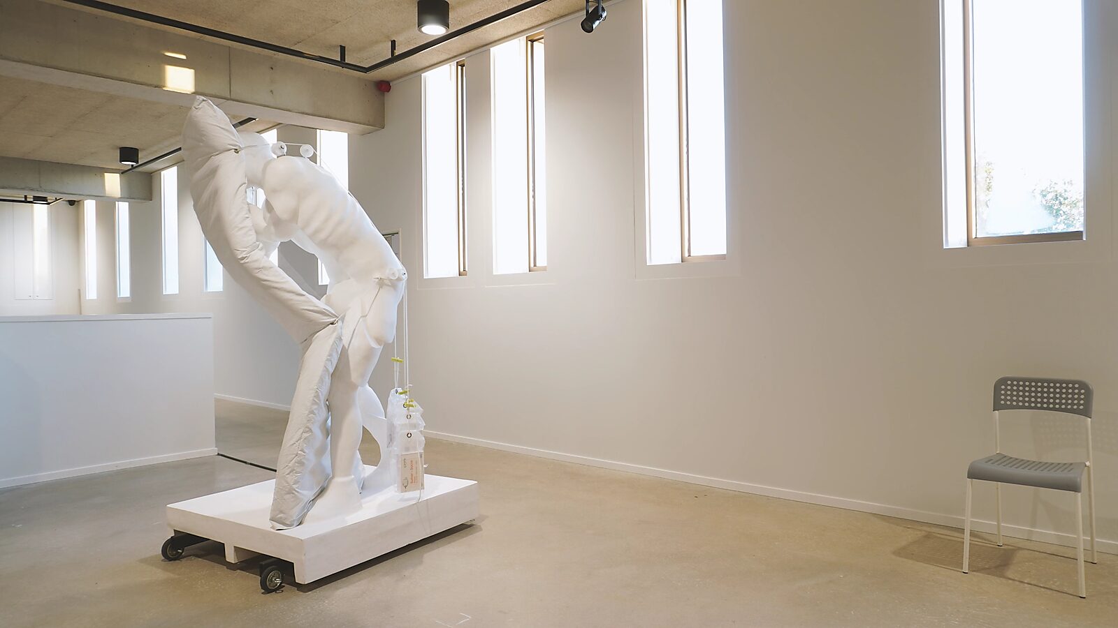 Sleeping In with the Sleepers — videostill of the artwork at the exhibition Transformation Studio No.1: Warm or Cold, CC De Adelberg Lommel: the air mattress partially deflates while the white sculpture continues leaning against it in a bent posture.