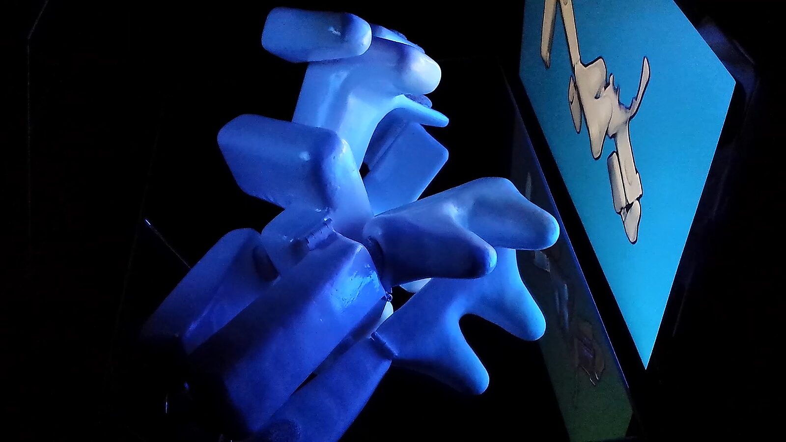 Reflections in Motion — videostill recording: the sculpture is lit in blue and appears multiplied through reflections, beside a screen showing a simplified contour of the form.
