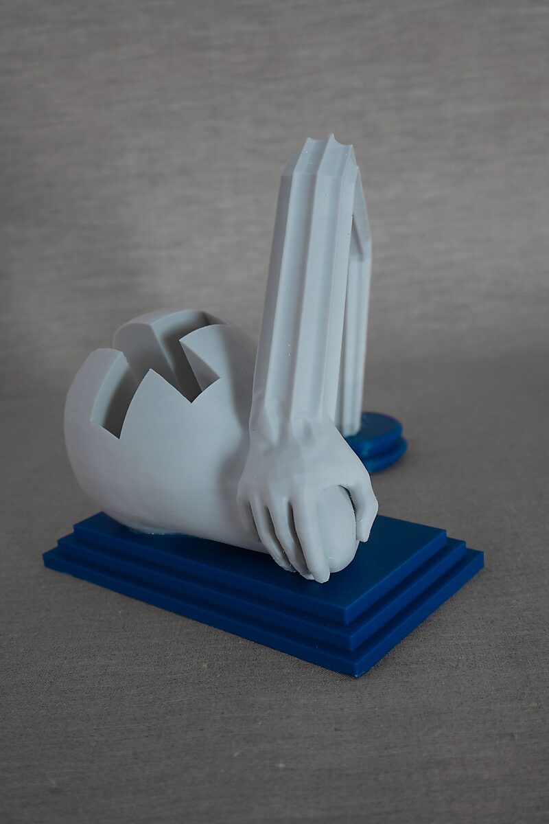 De zuilen van Ovidius — Arachne — 3D-geprinte sculptuur met een liggende figuur waarvan een arm uitloopt in een hoekige zuilvorm, geplaatst op een blauwe sokkel.