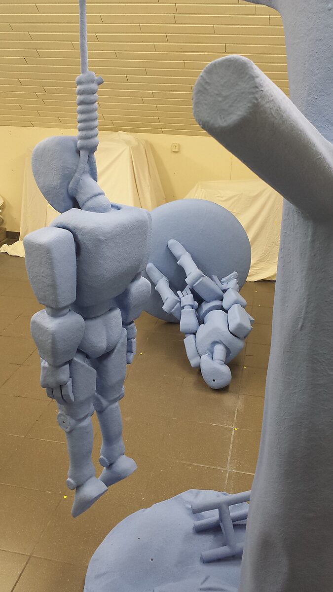 Robot in ontkenning — close-up van het hangende robotlichaam waarin de zachte monochrome afwerking het mechanische karakter contrasteert met een bijna menselijke kwetsbaarheid.