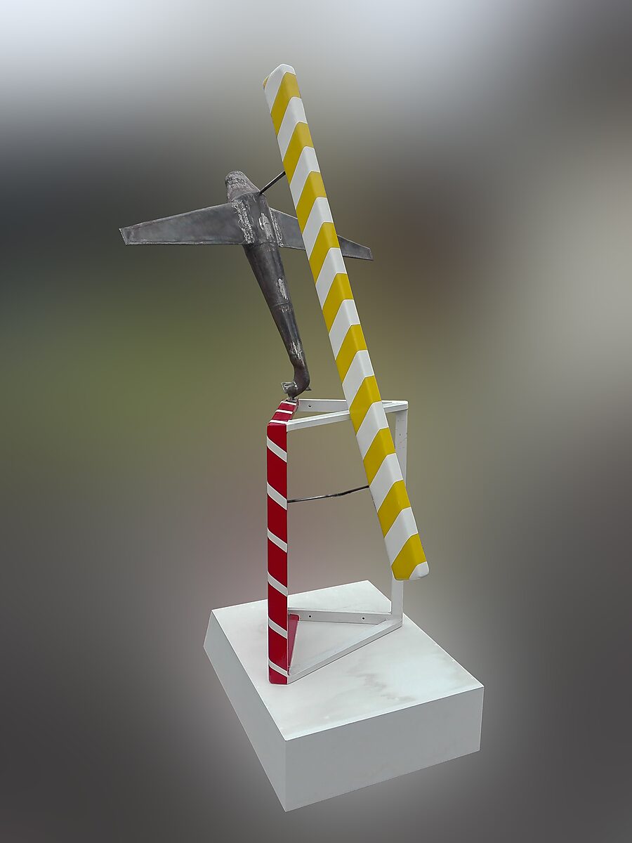 Faithful Airplanes — isolated view of a metal airplane sculpture resting on an open cube-like construction with contrasting red and yellow striped panels, presented on a white pedestal.