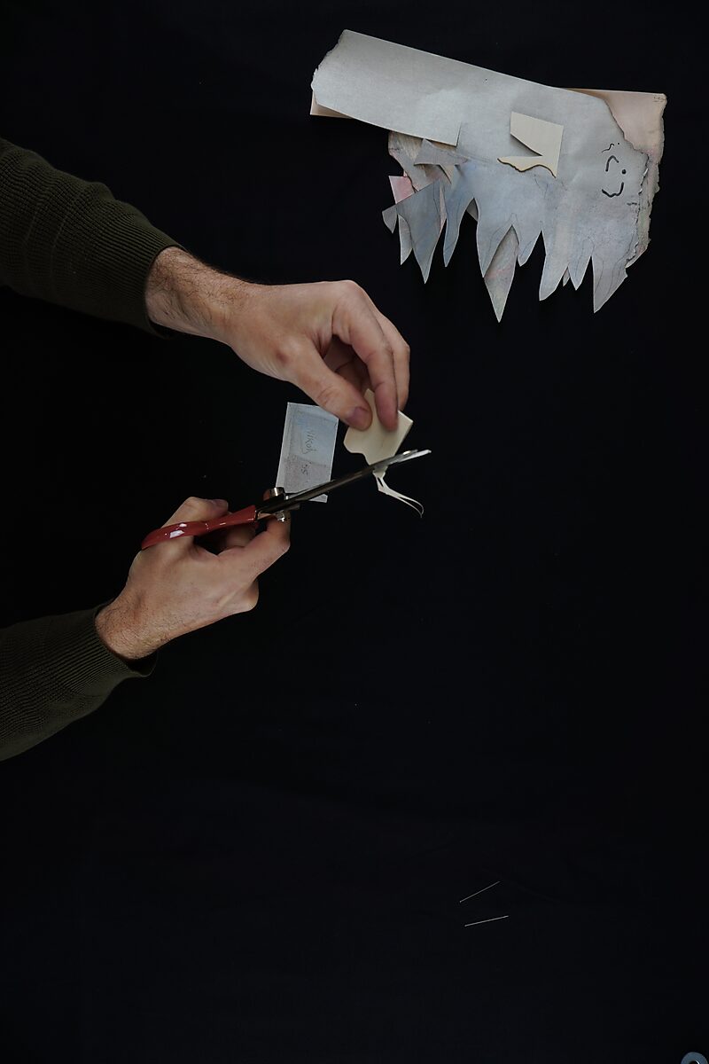 Naming–Value Butterflies — process drawing: Hanging Man (1995) — a small fragment is trimmed further with scissors; remaining pieces of paper lie scattered above.