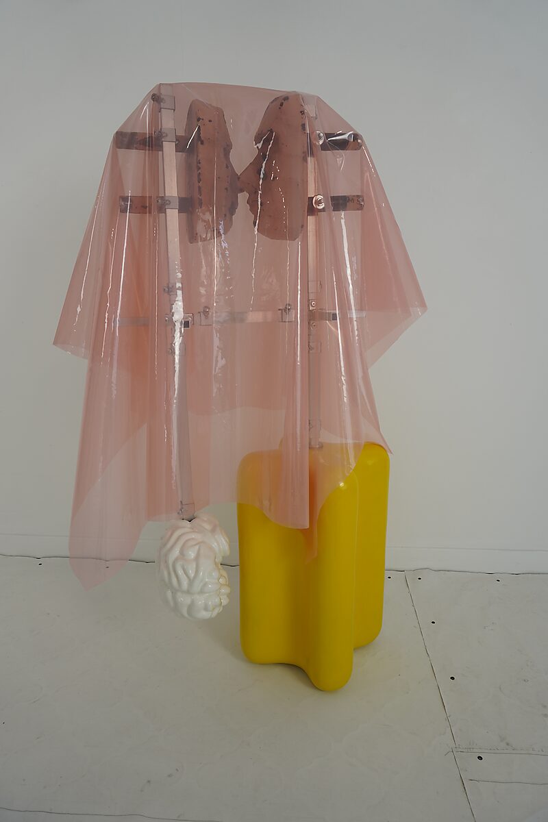 Choose and Change — studio setup of a sculpture with a yellow base form and transparent pink foil around a double head structure.