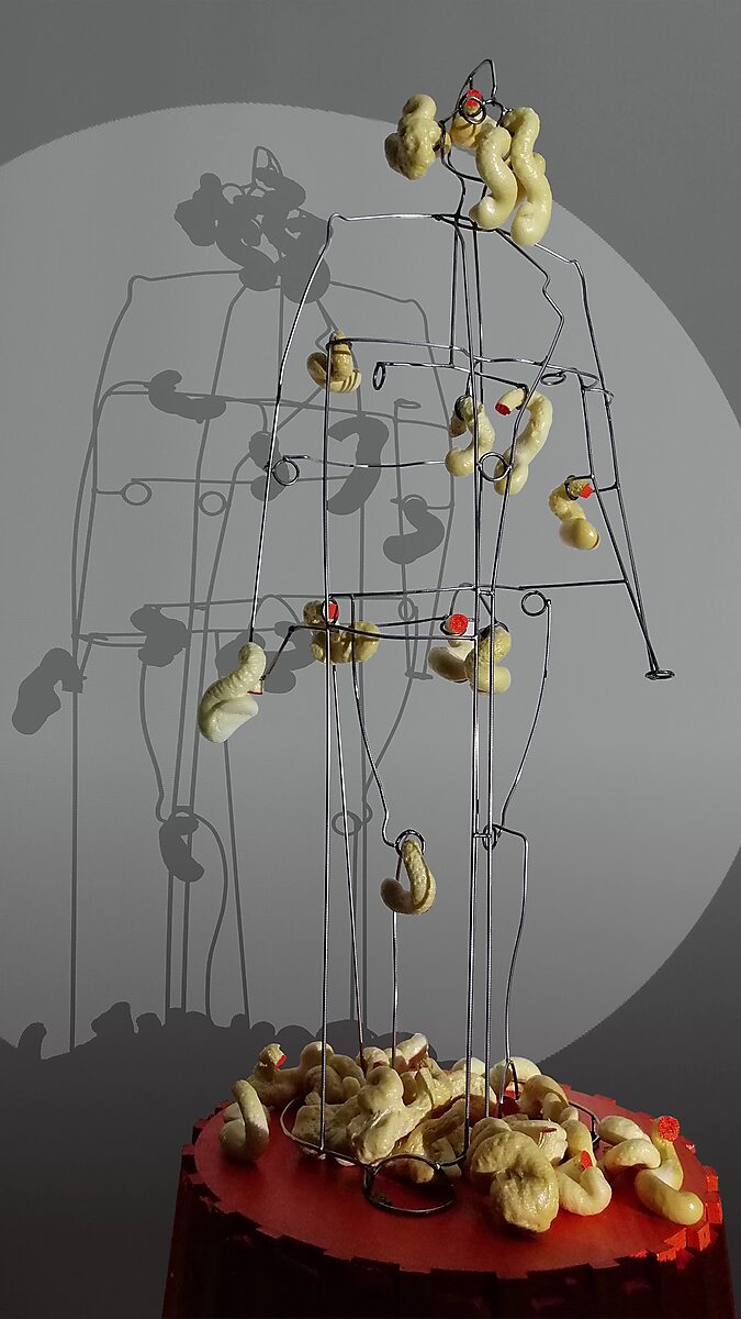 Sfincterman No.0 — videostill: the figure is surrounded by a swarm of hanging and falling forms, accumulating both on the body and on the platform.