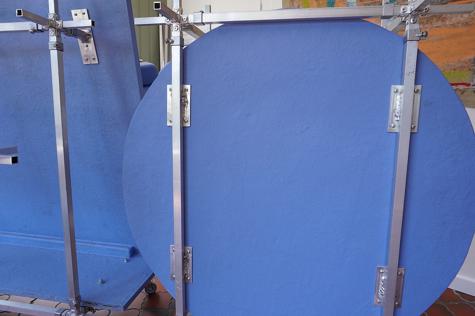 Kies en verander — aluminium constructiesysteem: grote blauwe panelen bevestigd aan een modulair metalen frame met gelaste verbindingen.