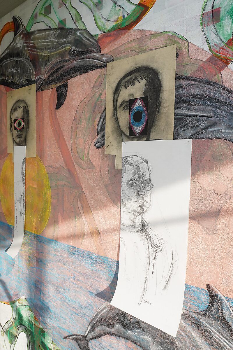 Naming–Value Butterflies — process drawing: self-portrait study (1995), Captured (2026) — a pencil self-portrait hangs below a charcoal portrait with a cut-out eye shape on a painted drawing board with dolphins.