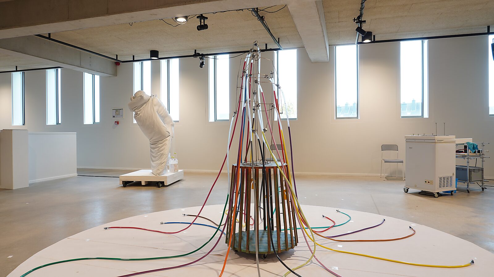 Sfincterman with Colour Tentacles — exhibition view: multiple colored tubes spread radially around the sculpture, forming a network of lines across the floor.