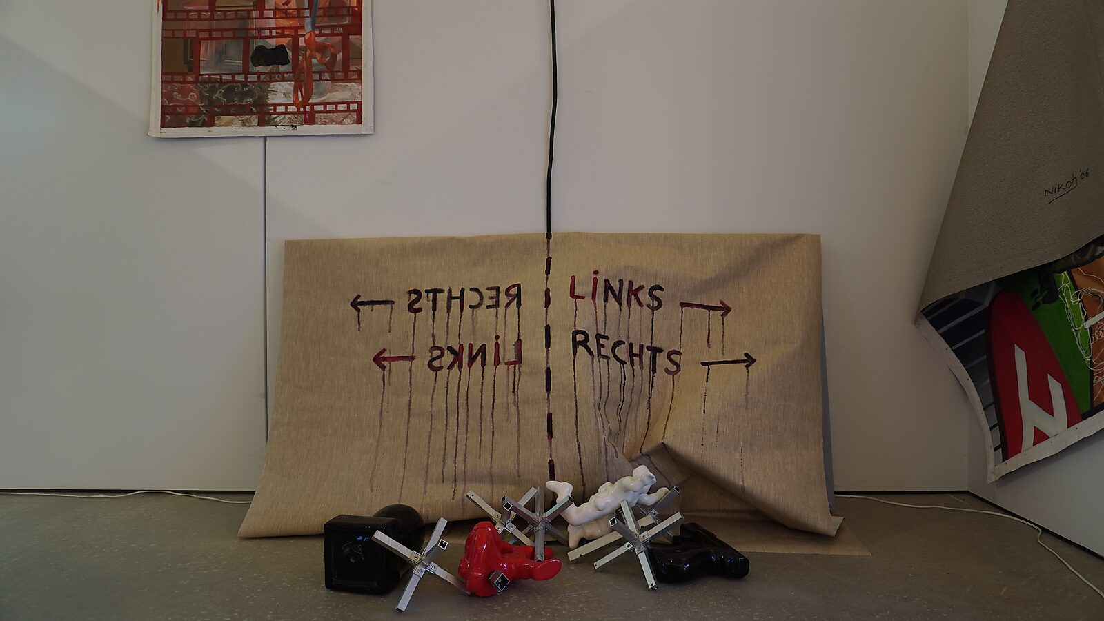 De Verdeler — The Divider — procesfoto: variatie op de tentoonstelling — het doek met “links / rechts” staat op de grond met sculpturen en objecten ervoor.