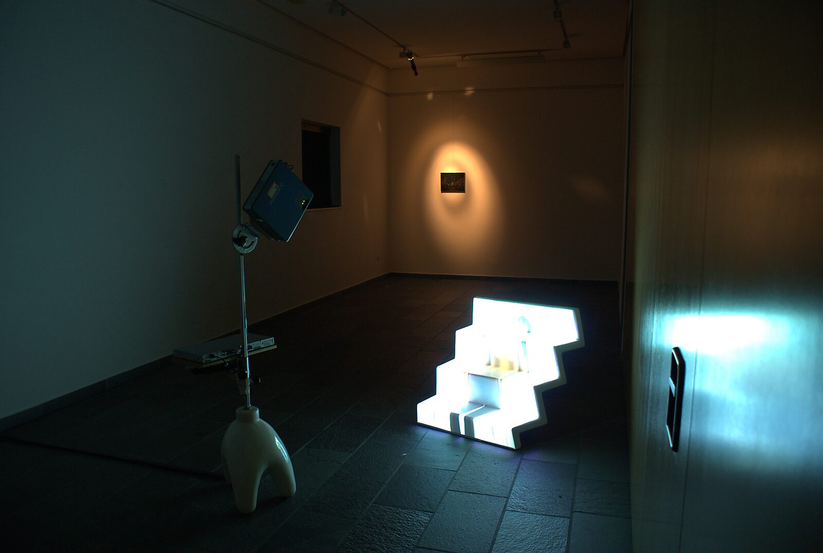 ‘Pro-Life’: Tentoonstellingszicht met verlichte witte sculptuur; spotlicht op een klein schilderij aan de muur, CC De Adelberg, Lommel, 2015.