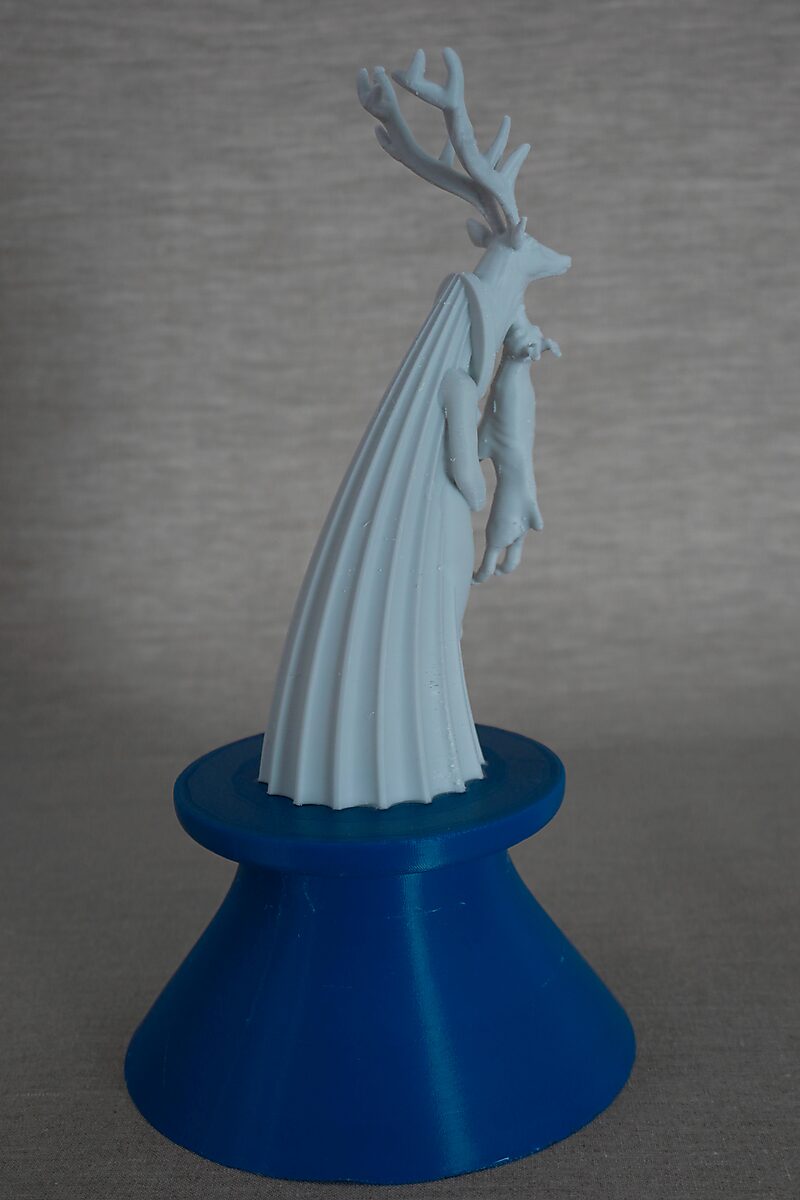 The Columns of Ovidius — Actaeon — side view of a 3D-printed figure with a deer head, draped form and antlers, placed on a blue pedestal.