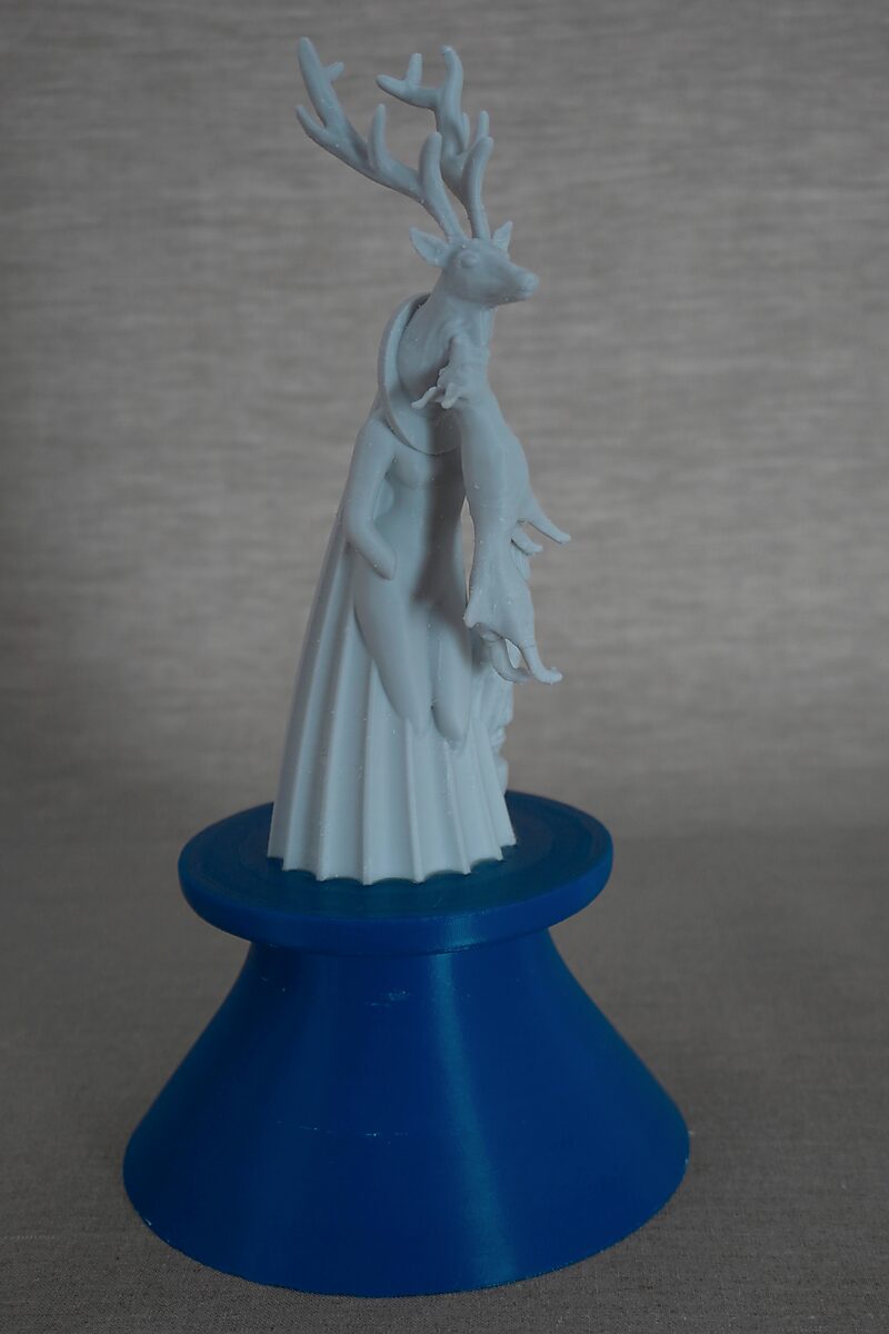 De zuilen van Ovidius — Acteon — 3D-geprinte sculptuur van een figuur met hertenkop en gewei, staand op een blauwe sokkel en een dierlijk lichaam vasthoudend.