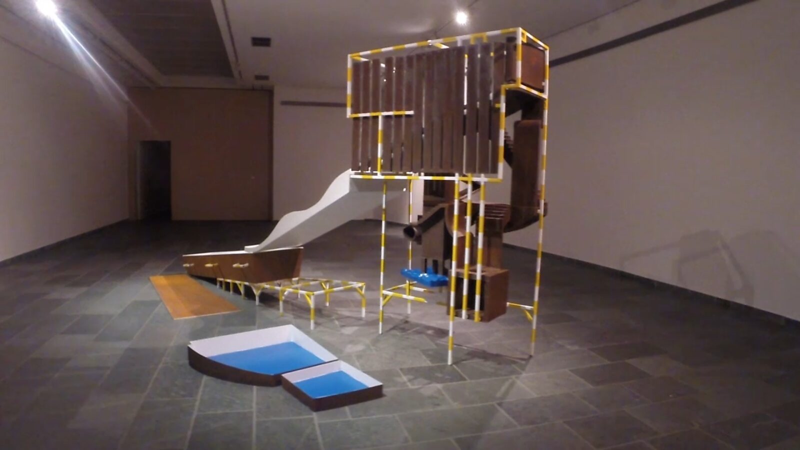 Construction with Blue — video still in which a labyrinth-like structure of rusted metal planes and vertical elements represents a phase of orientation and wandering within the line of life.