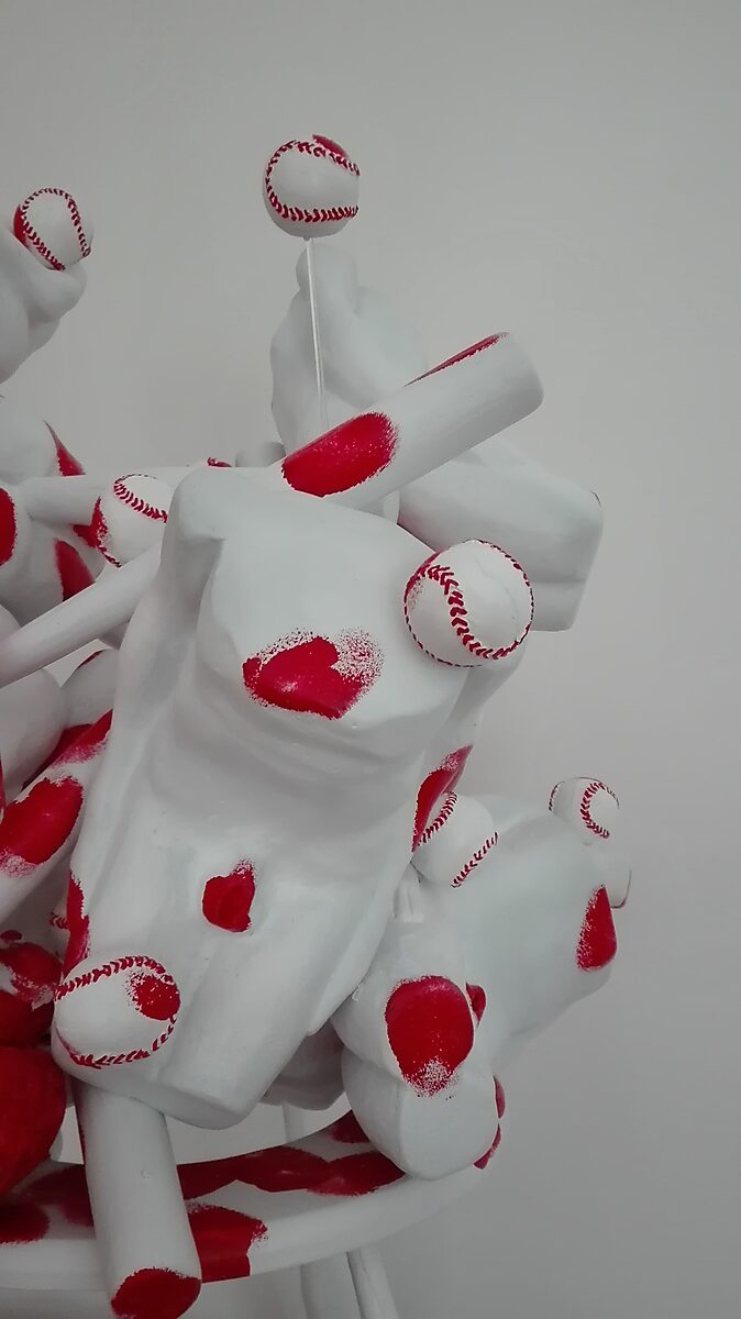 Butt’s, Bats and Balls — detail showing a body fragment pierced by a baseball bat while suspended baseballs suggest arrested kinetic energy.