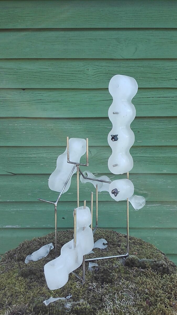Entropic Sculpture No. 1 — videostill of the sculpture in spring with partially melted ice and pieces of ice on the moss around the metal armature.