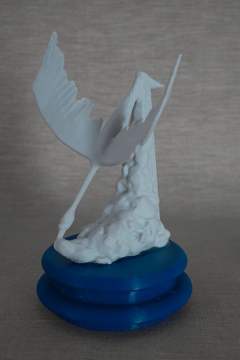 De zuilen van Ovidius — Cycnus — 3D-geprinte sculptuur met een vogelachtige figuur met gespreide vleugels naast een verticale zuilvorm op een ronde blauwe sokkel.