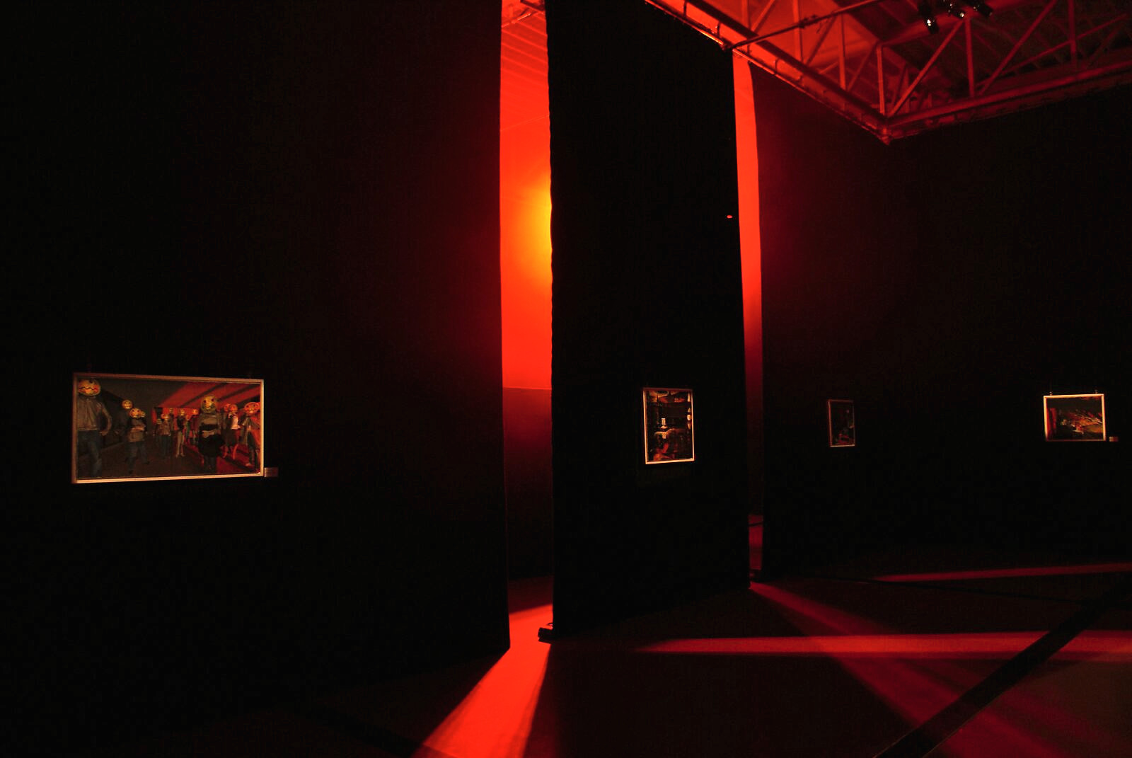 The Modern Cavemen — overview of the darkened space where individual works appear as luminous windows between the curtains; the scenography enhances the sense of a contemporary cave.