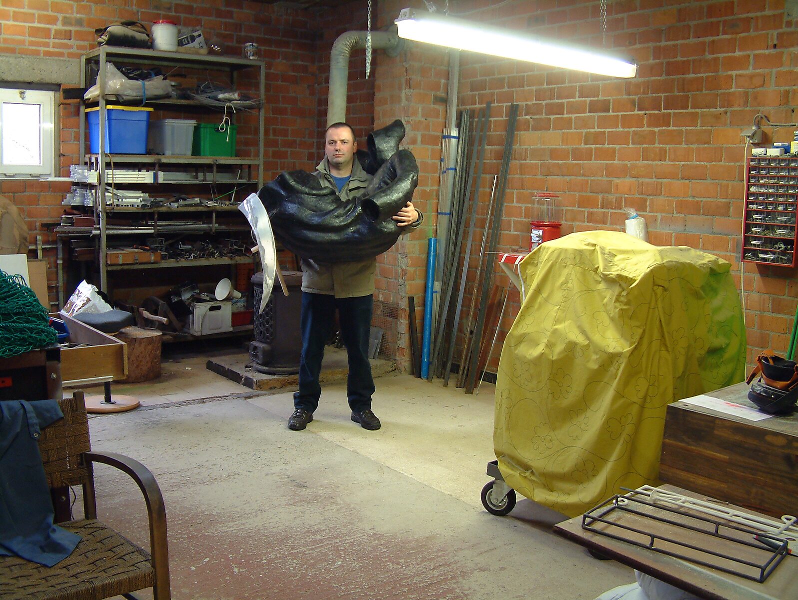 Doodsval nr. 1 en nr. 2 — de kunstenaar draagt een sculpturale figuur van Pietje de Dood in een atelierruimte, omringd door werkmateriaal en gereedschap.