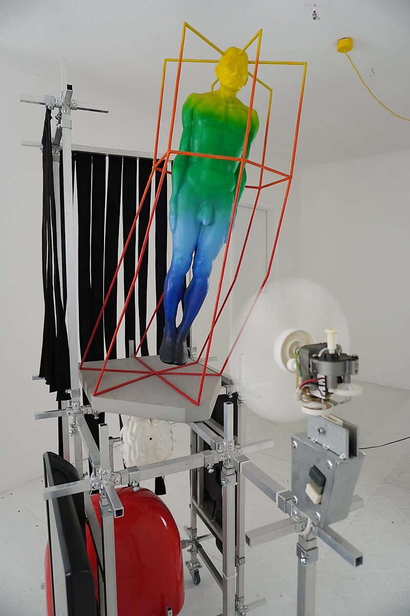 Thermiekbelofte — de draaiende ventilator blaast lucht langs het sculptuur Gedachtenkooi, waardoor een relatie ontstaat tussen mechanische energie, lichaam en omgeving.