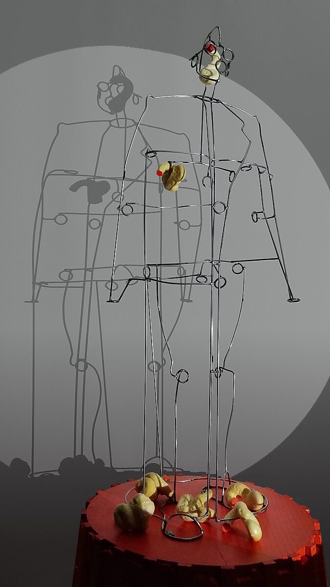 Sfincterman No.0 — videostill: initial lumps of yellow, foam-like material appear on the body and fall around the figure’s feet.