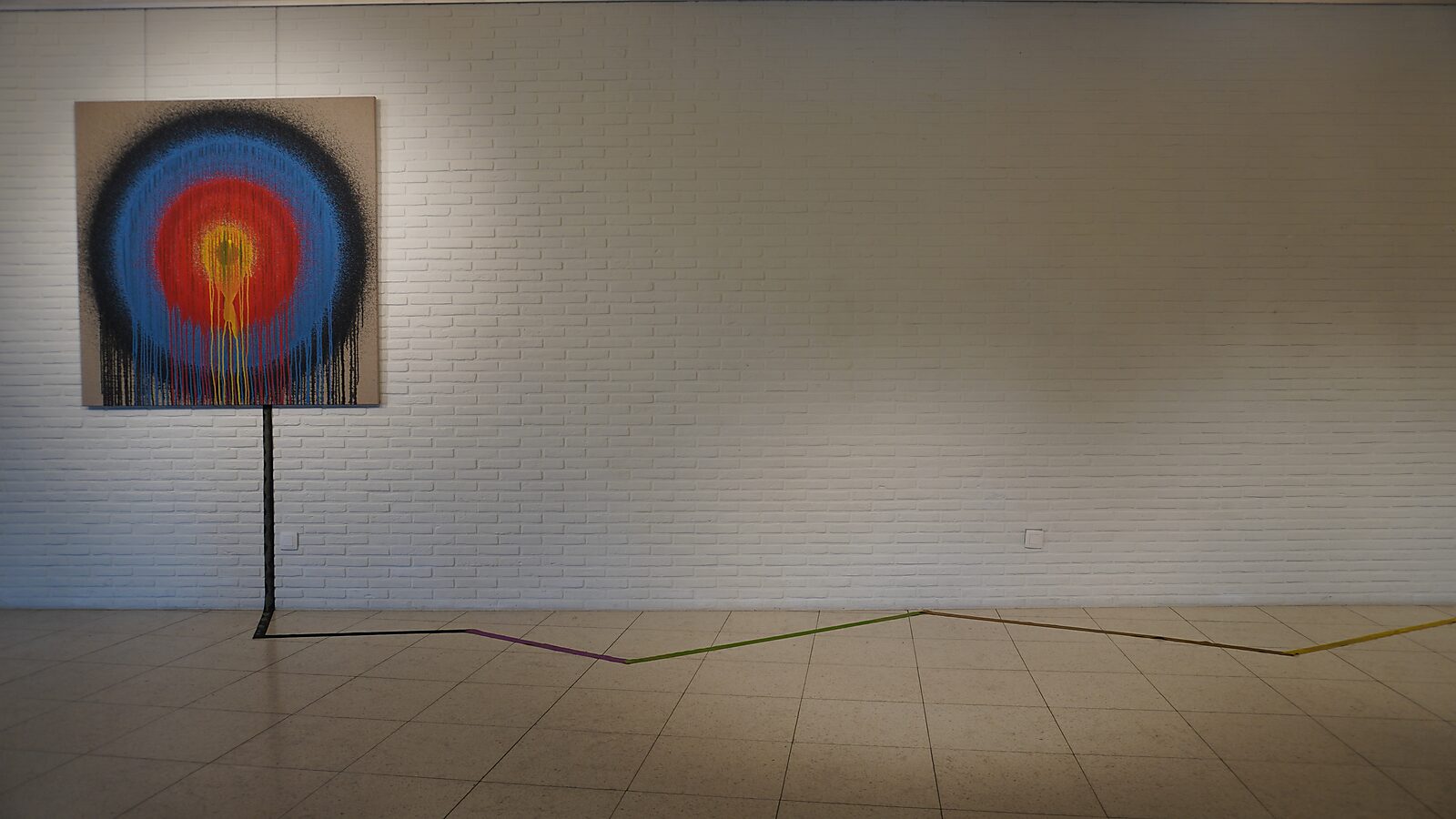 'Sfincterman for President’: Exhibition view with a target-like canvas in black, blue, red and yellow; a line extends from the canvas and continues across the floor, Dommelhof, Pelt, 2024.