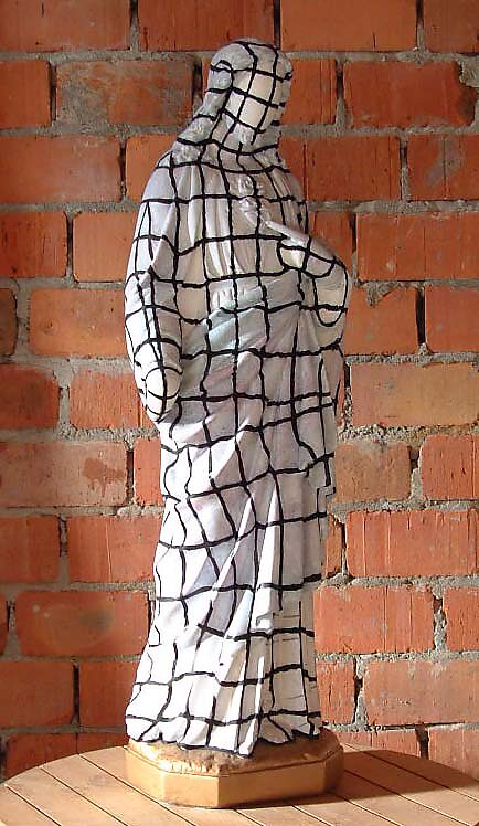 Raster Christ — sculpture of a traditional Christ figure whose surface is covered with a black grid resembling a 3D wireframe; the classical religious image is thus read as a body in transition, as if faith shifts from material devotion toward a digital, 