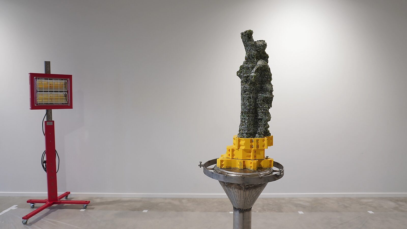 ‘Transformatiestudio nr.1: warm of koud’: Exhibition view with a white-and-green speckled sculpture, a yellow mold and a stainless-steel plinth, CC De Adelberg, Lommel, 2024.