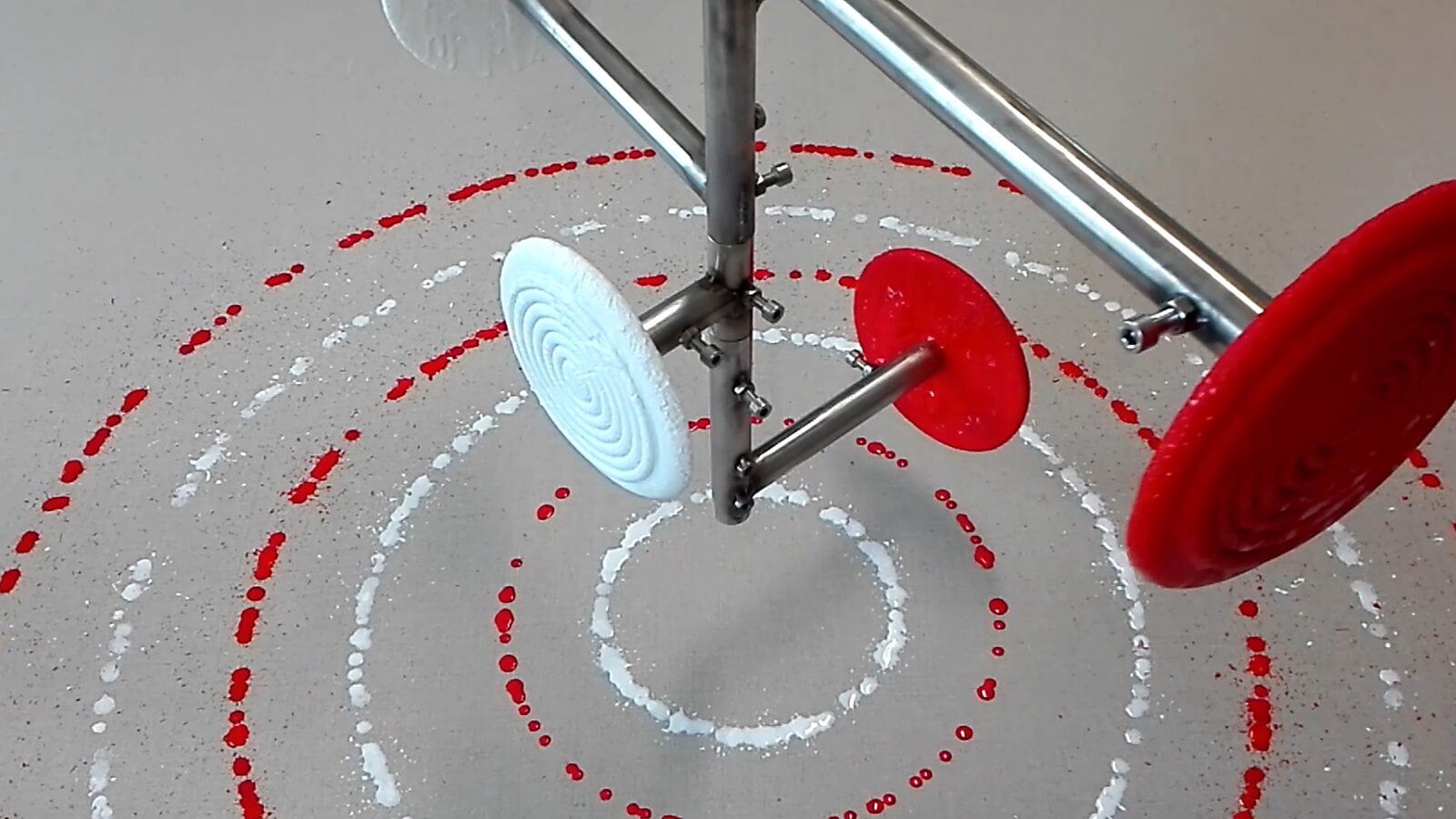 Melting Targets No. 3 — video still of rotating ice targets mounted on a metal armature above a canvas where red and white drip circles appear.