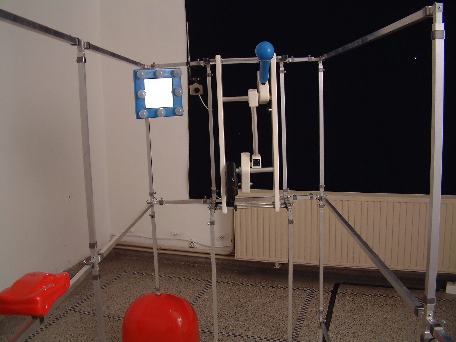 Choose and Change, Installation for a Selfish Rapper — photo of the installation: metal frame construction with mechanical elements and an illuminated square panel, set in an exhibition space.