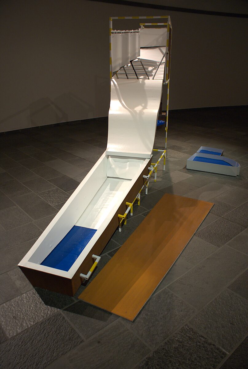 ‘Pro-Life’: Tentoonstellingszicht van witte glijvorm verbonden met een verhoogde metalen constructie; blauwe en houten elementen op de vloer, CC De Adelberg, Lommel, 2015.