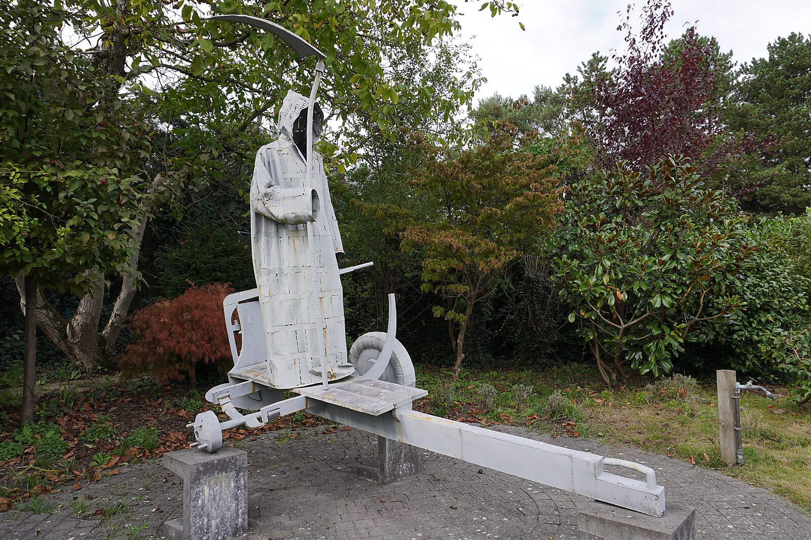 Interrupted Crossing — sculpture of Death as ferryman on a boat trailer installed in a garden environment, shown in full side view.