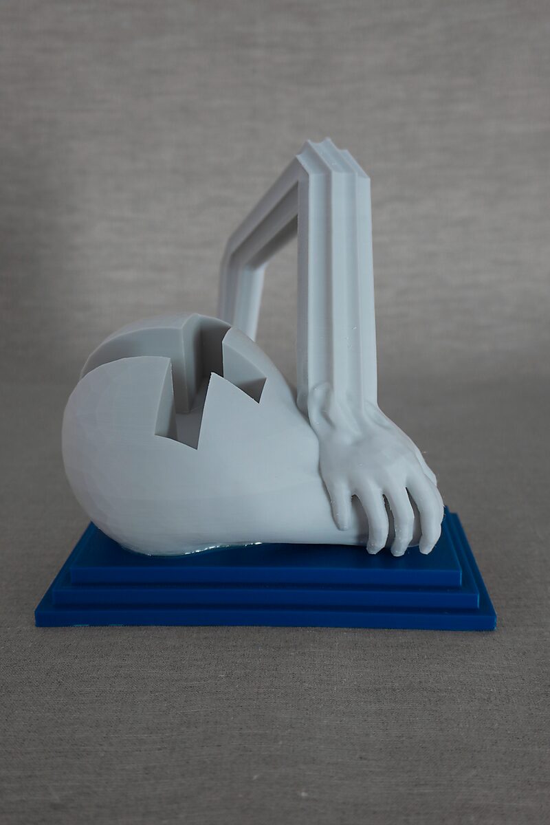 The Columns of Ovidius — Arachne — opposite side view of a reclining 3D-printed figure with a hand form and angular column structure on a blue pedestal.