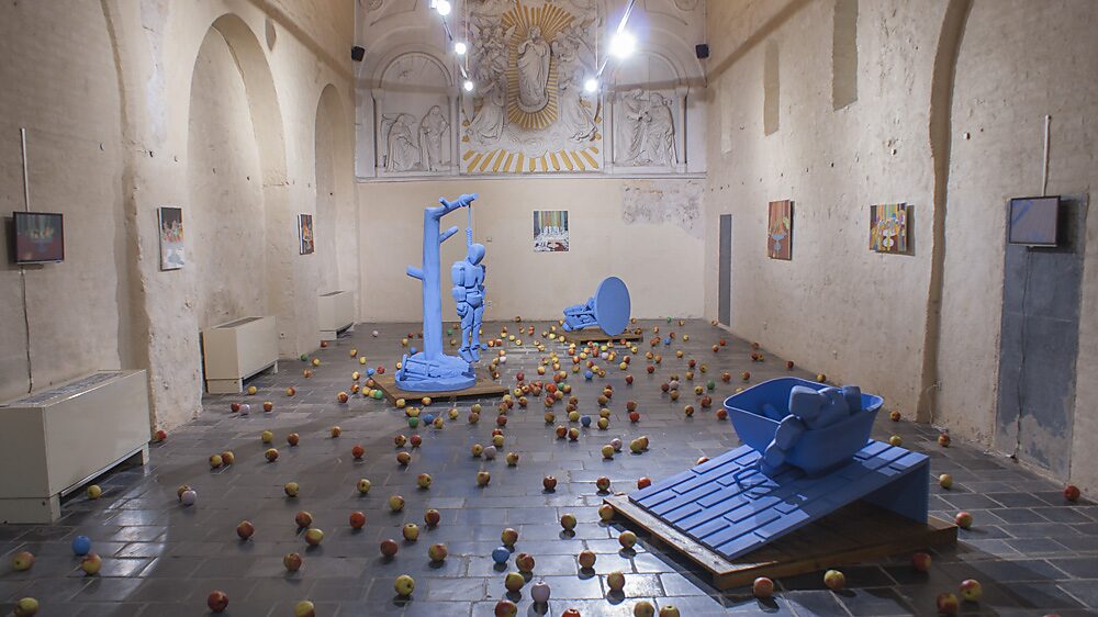 Strange Fruit — totaalopstelling van meerdere robotsculpturen in de kapelruimte, gecombineerd met een schilderijenreeks van fruitschalen en een vloer bedekt met appels, waardoor een associatie ontstaat tussen stilleven, lichaam en val.