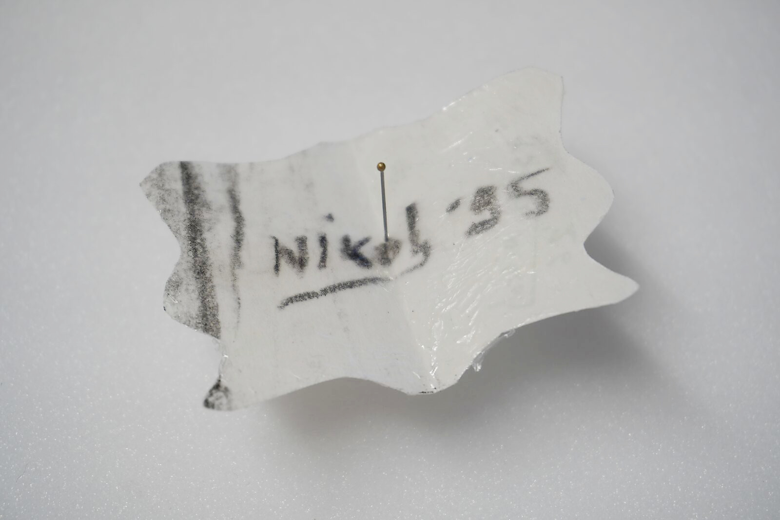Benoemens-waardvlinders — Naming–Value Butterflies — proces tekening: studie zelfportret (1995), Gevangen (2026) — vlindervormig stukje papier met de handgeschreven naam “Niko ’95”, vastgezet met een speld.