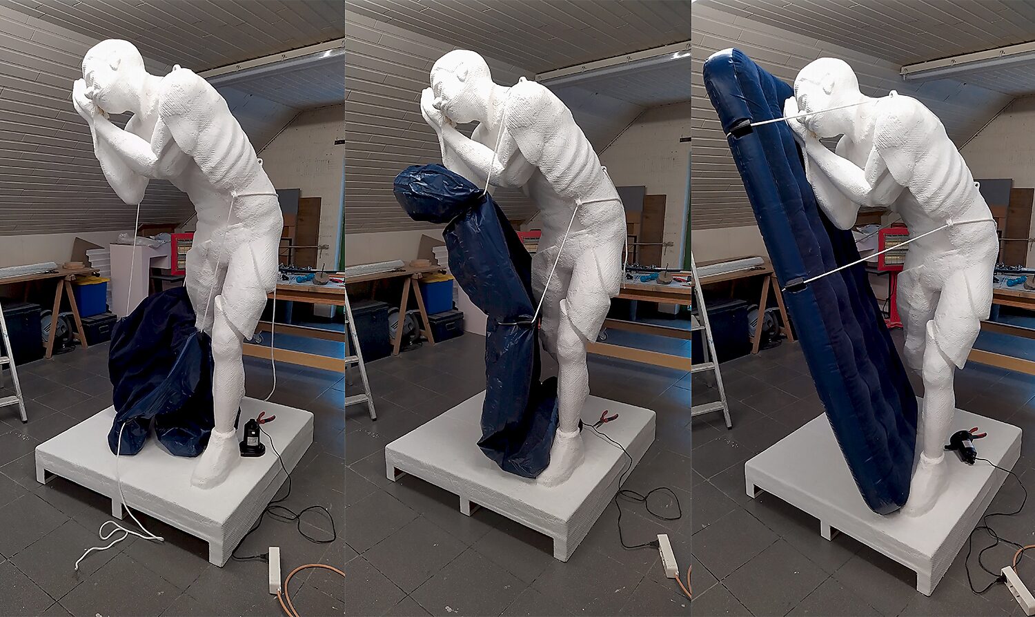 Uitslapen met de slapers — studiefoto van het kunstwerk tegen een zwarte achtergrond: het witte beeld van een gebogen figuur drukt tegen een groot luchtmatras dat naar voren helt.