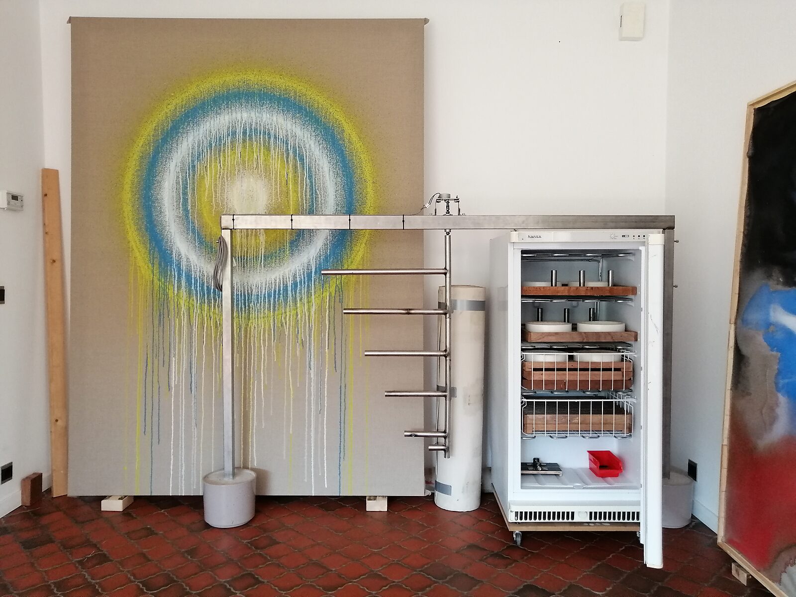 Smeltende doelen nr. 3 — atelieropstelling met metalen constructie, groot doek met concentrische kringen en een diepvriezer met mallen voor de ijsdoelen.