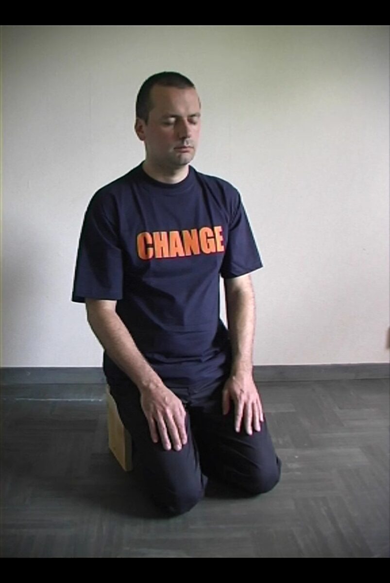 Choose and Change no. 2 — video still of the artist kneeling on the floor, in a still pose with closed eyes and the word “CHANGE” on the T-shirt.
