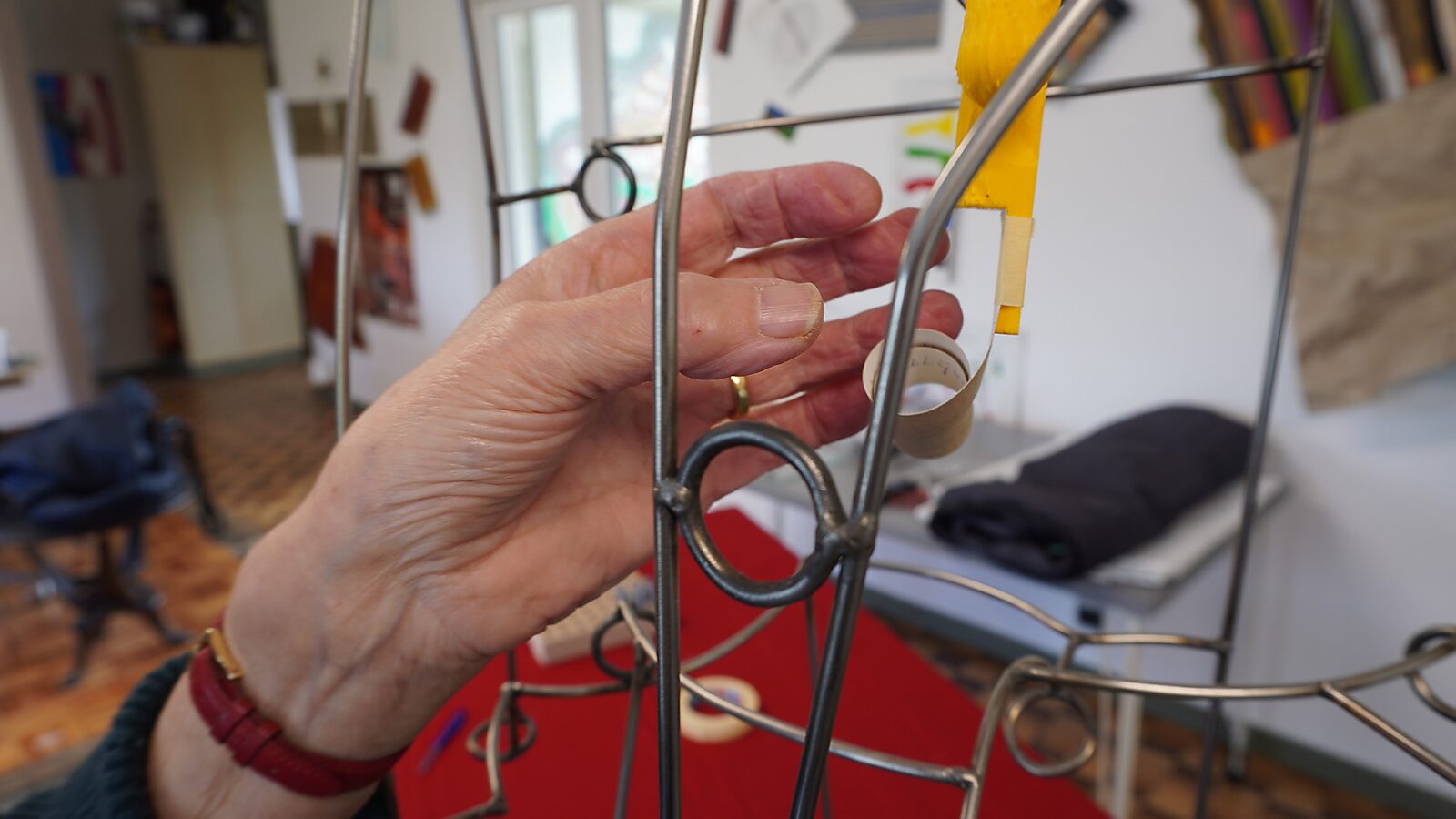 Sfincterman nr.0.0 — videostill handeling: de hand laat het object los zodat het vrij aan de metalen structuur hangt, met de papieren strook zichtbaar bungelend.
