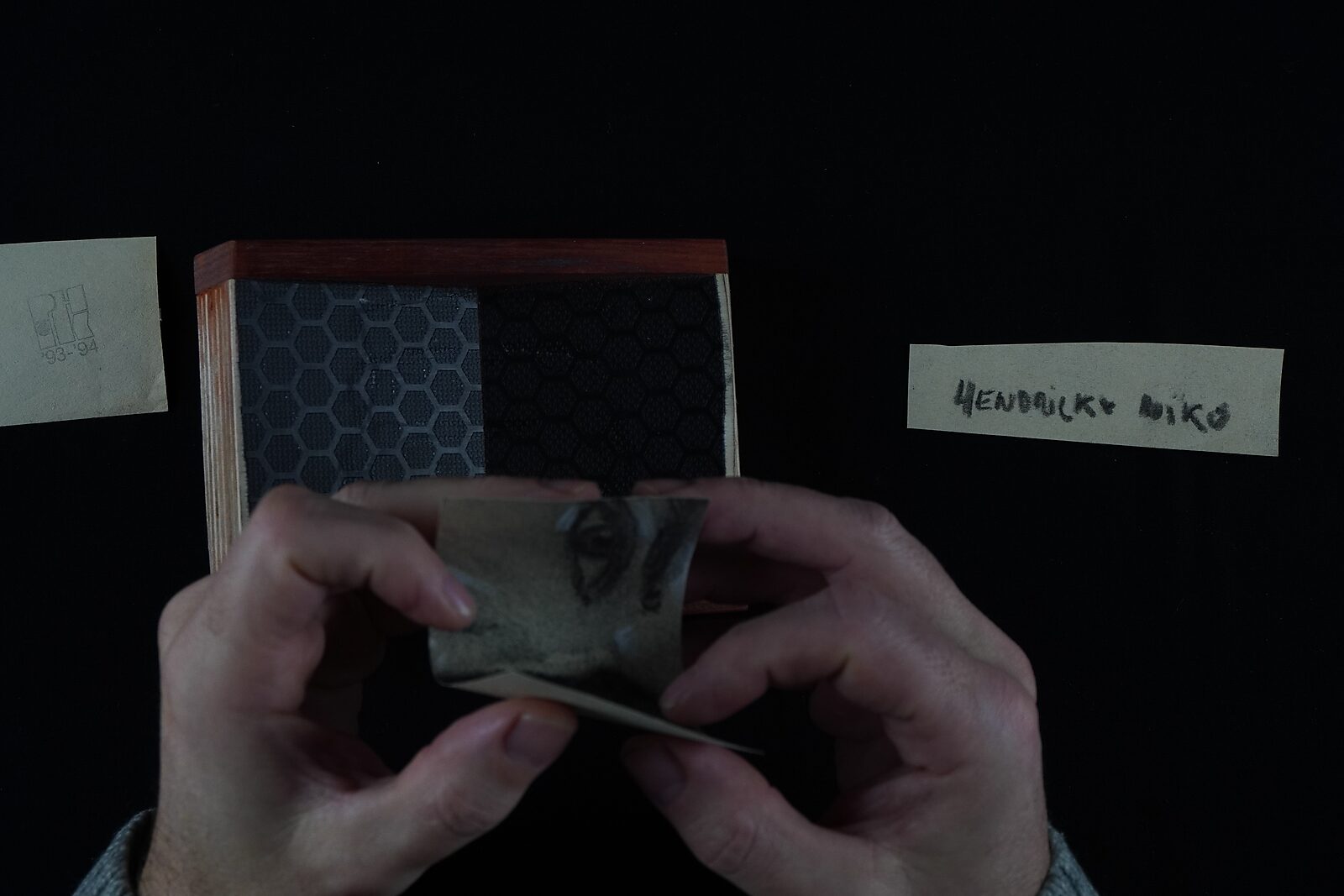 Benoemens-waardvlinders — Naming–Value Butterflies — proces tekening: studie zelfportret 2 PHIKO (1993), Gevangen (2025) — handen buigen het kleine fragment met de ogen boven een open doos.