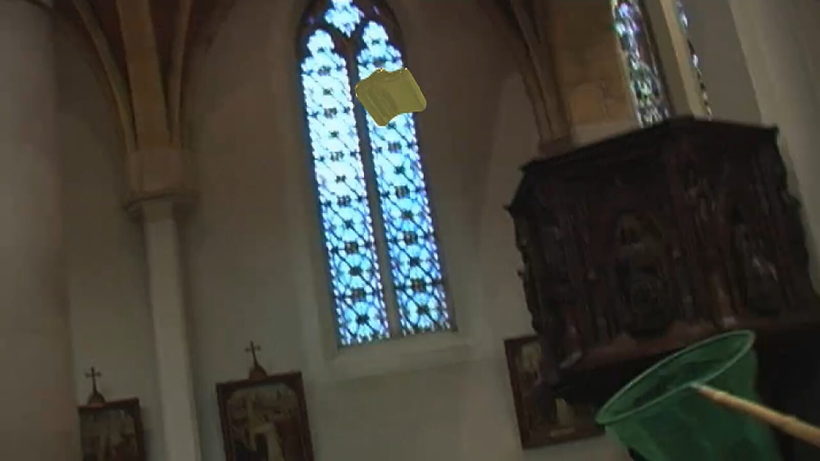 Kies en verander, De vanger van het kruis — videostills: schuin camerastandpunt in een kerk met glasraam, een gouden kruis zweeft en een groen net verschijnt onderaan rechts.