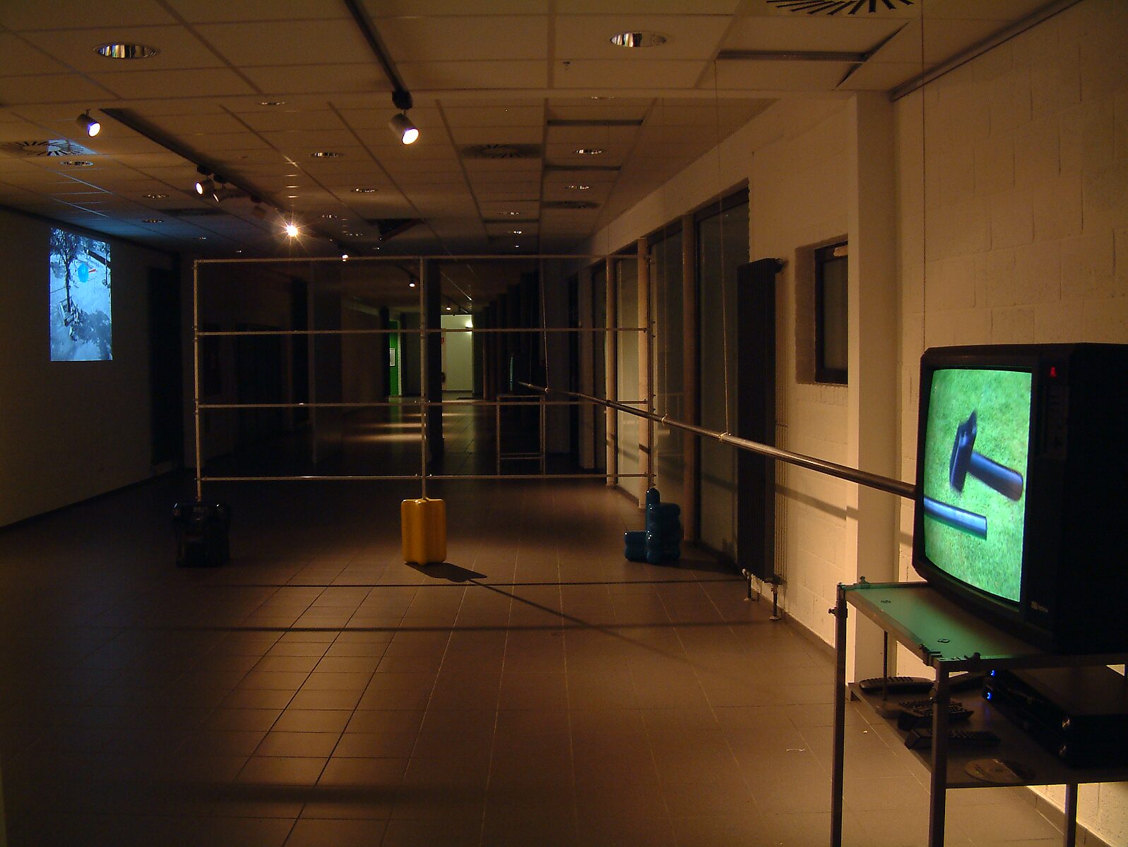 'Kies en verander project’: Tentoonstellingszicht van lange gang met televisiemonitor op tafel; metalen buisstructuur met gekleurde voetstukken in geel en blauw, CC De Kollebloem, Puurs, 2008.
