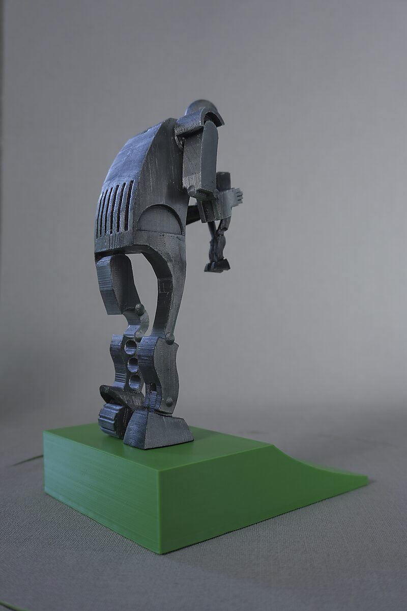 Saturnus — zwarte 3D-geprinte miniatuur in zijaanzicht van een gebogen figuur die een kleinere figuur naar beneden houdt, op een groene sokkel.