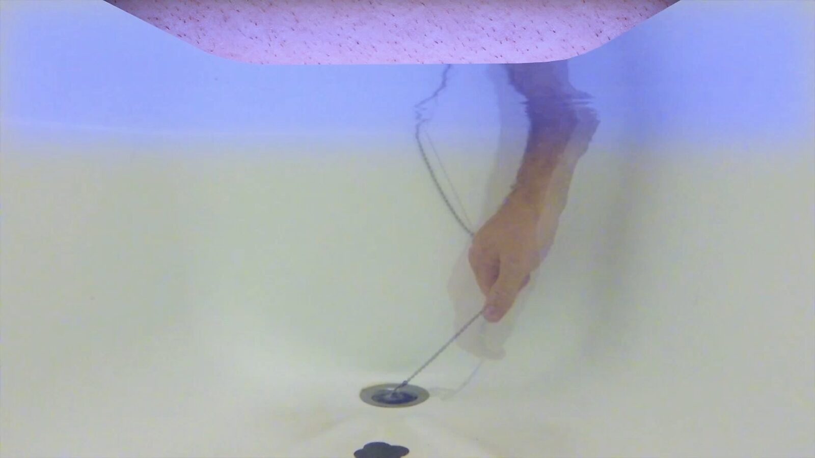 Imaginary Landscapes — video still showing a human hand pulling a drain plug from a bathtub, an action functioning as a metaphor for shutdown, reset, or interruption of a system.