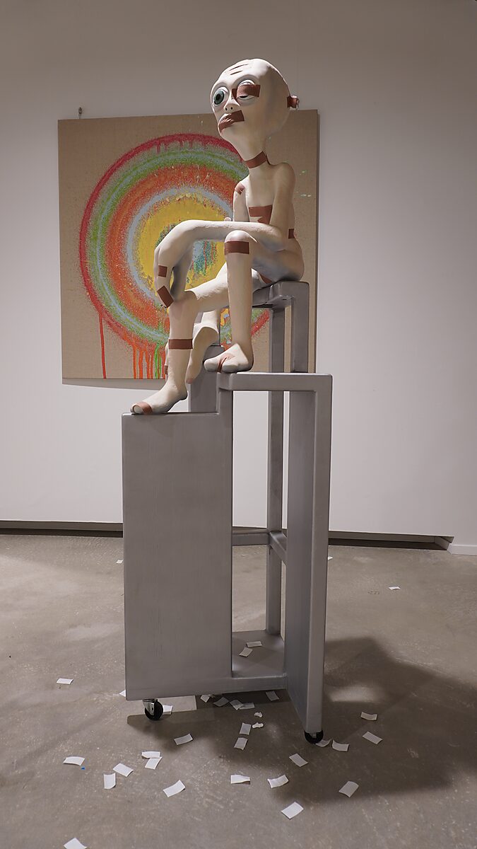 Alien Care, Bandage Phase 1 — front view: alien figure with bandages seated on a tall geometric chair; small white paper pieces scattered on the floor.