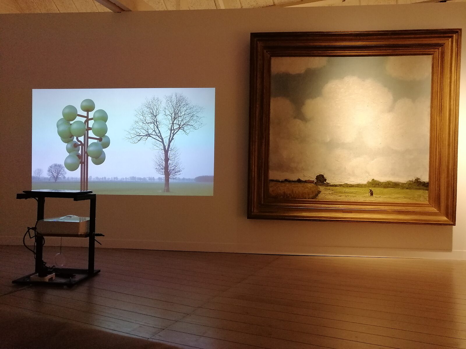 ‘Oog in Oog’: Exhibition view with projection of a stylised tree next to a landscape painting by Jakob Smits in a wide gilded frame; wooden floor and dimmed gallery space, Jakob Smits Museum, Mol, 2019