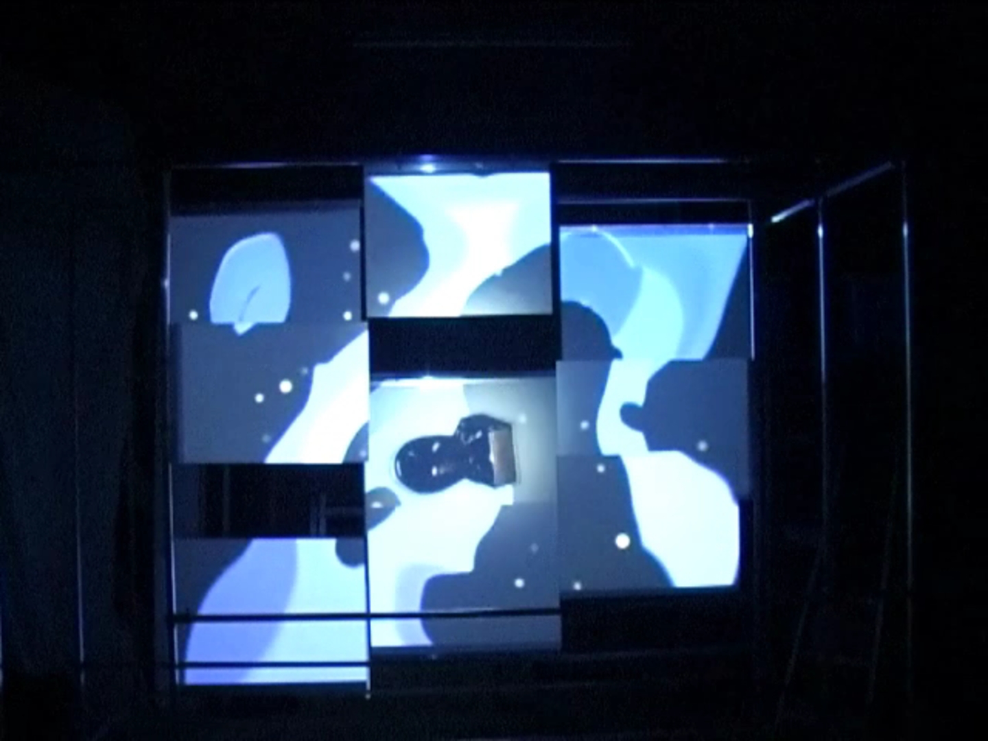 Vloeibare vormen doorheen de ruimte — videostill van de installatie waarin blauwe en witte vloeibare vormen over de panelen bewegen en door de verschoven schermvlakken in fragmenten worden verdeeld.