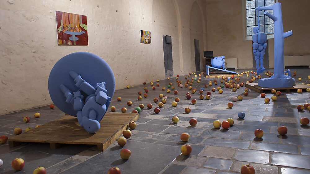 ‘Strange Fruit’: Exhibition view with a blue robot figure lying on a platform; real apples scattered across the floor (some painted), paintings on the wall, Gasthuiskapel, Borgloon, 2015.
