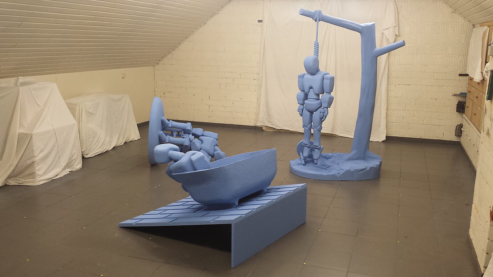 Robot in Denial — studio installation showing three sculptures in which a robot figure appears in different situations of self-destruction, arranged as a fragmented narrative about loss of control and existential denial.