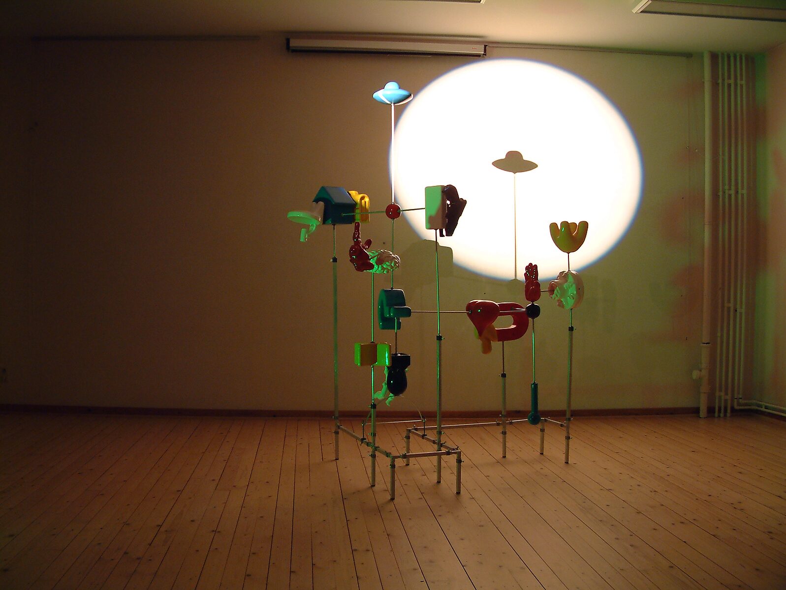 ‘Zien’: Tentoonstellingszicht met kleurrijke sculpturale installatie op metalen buisstructuur; ronde lichtprojectie op de wand achter het werk, CC De Breughel, Bree, 2006.
