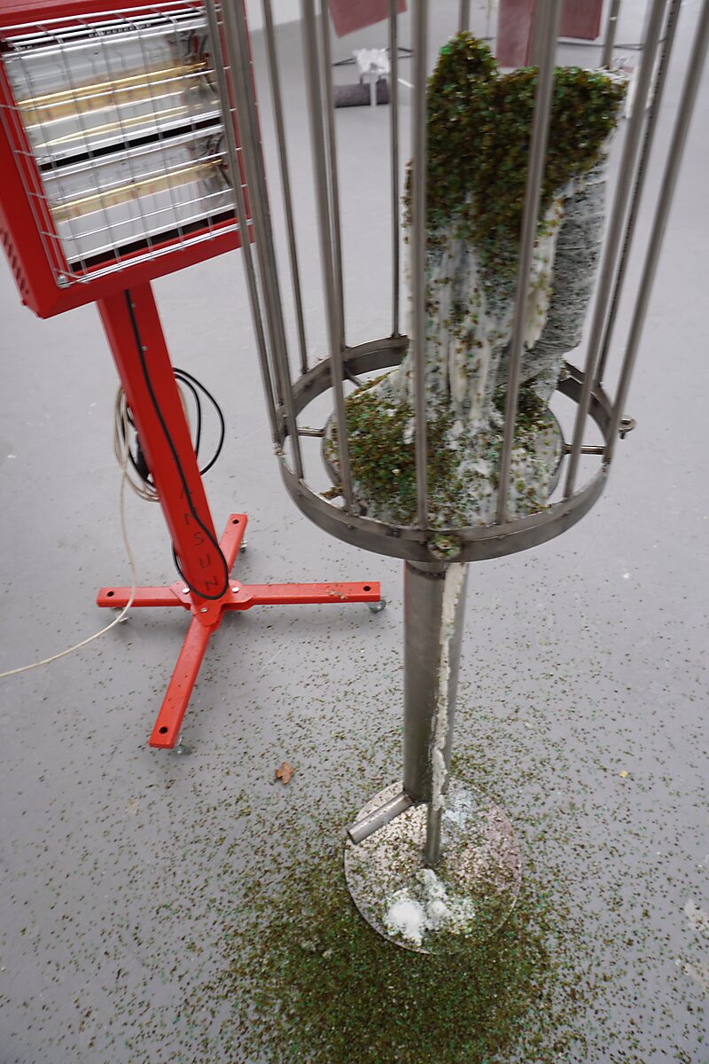 The Great Escape of Saint Sebastian — infrared heater beside the cage warms the sculpture while melted fat and glass beads drip downward.